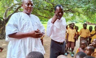 Two officials speak with pupils under a tree at a school compound